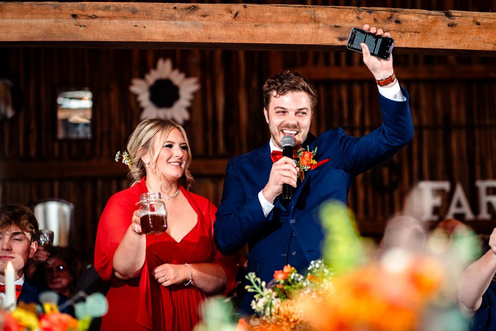 Wedding guests raise glasses during joyful toasts at rustic barn reception with colorful floral decor.