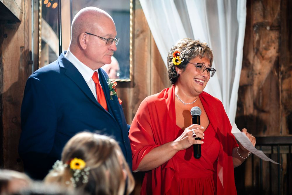 Speakers share emotional moments during wedding speeches in rustic barn venue.