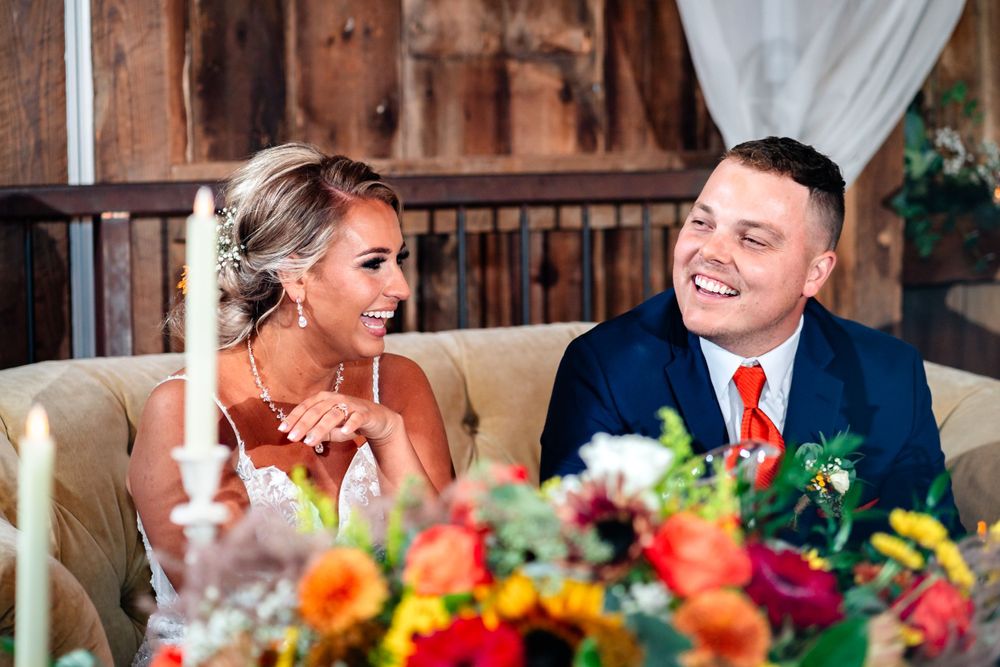 Couple shares laughter at reception table decorated with vibrant autumn flowers.