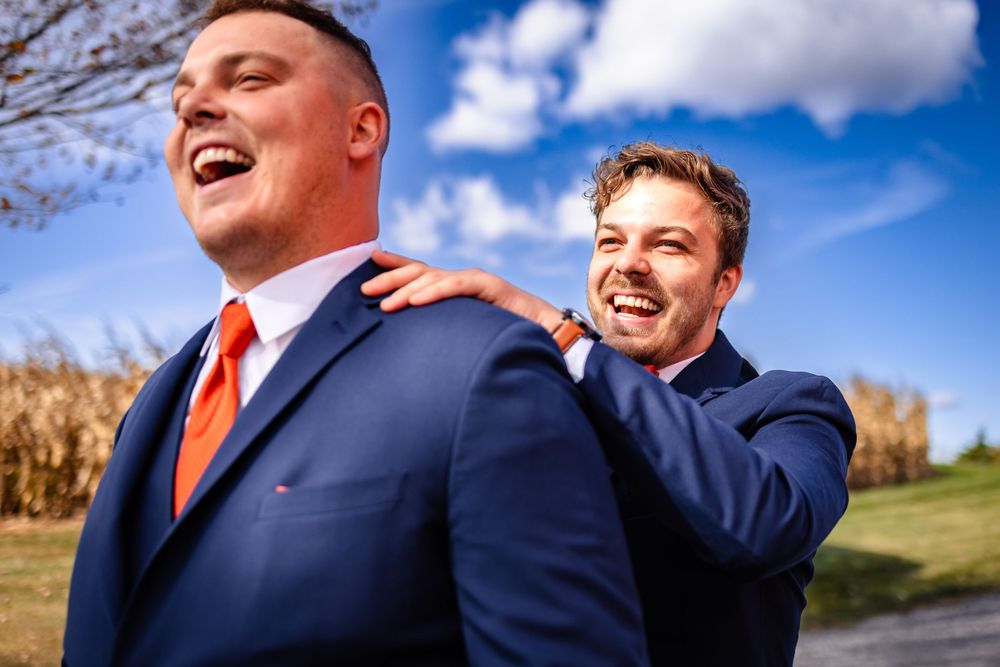 Groomsmen in navy suits and orange ties posing outdoors against blue sky.