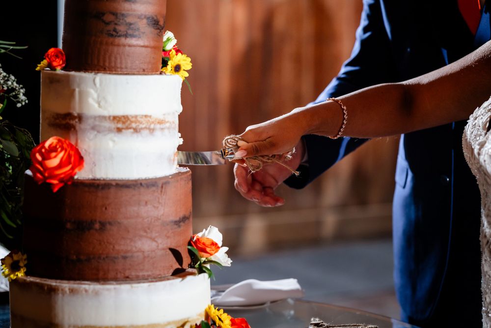 Close-up of knife cutting into tiered wedding cake decorated with orange and red flowers.