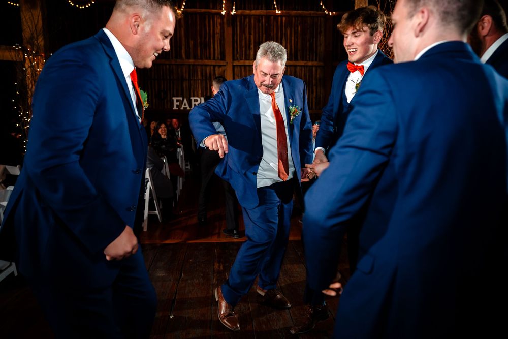 Wedding guests dancing and celebrating at a rustic barn reception with warm lighting and festive atmosphere.