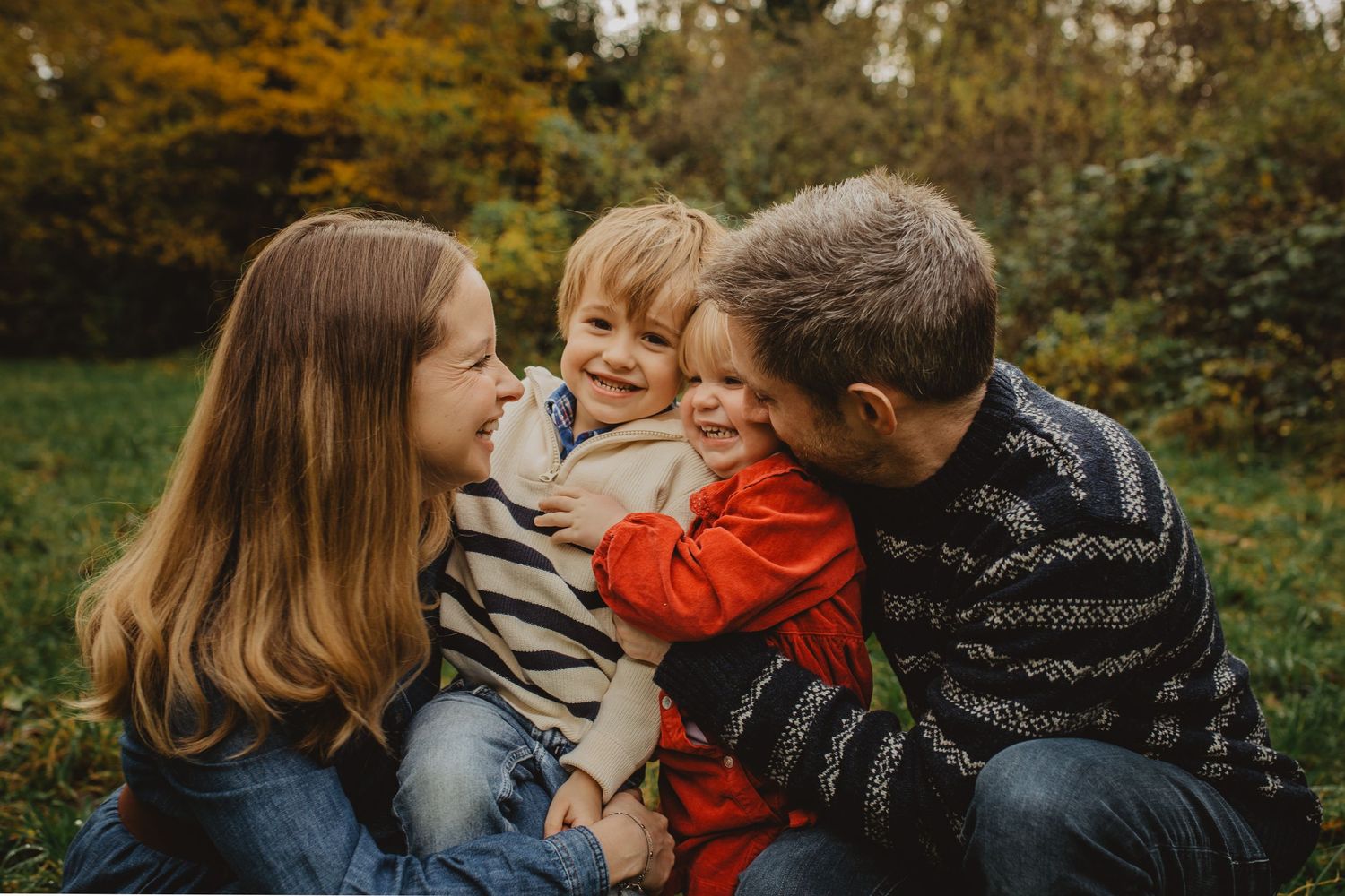A family in coordinating red and brown outfits poses together outdoors near a white fence during a photo session.