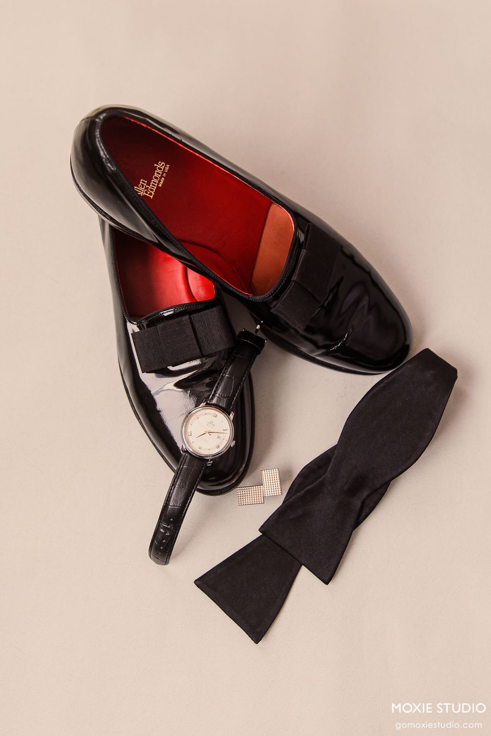 Black leather dress shoes with tassels arranged in sequence on beige background.