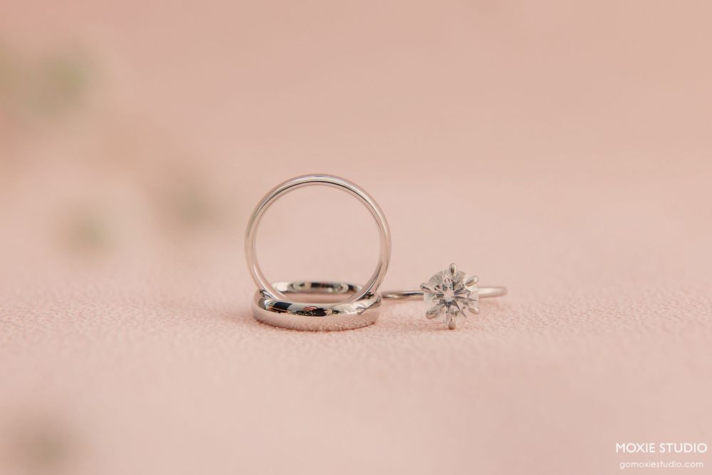 A delicate engagement ring with a solitaire diamond sparkles against a soft pink background.