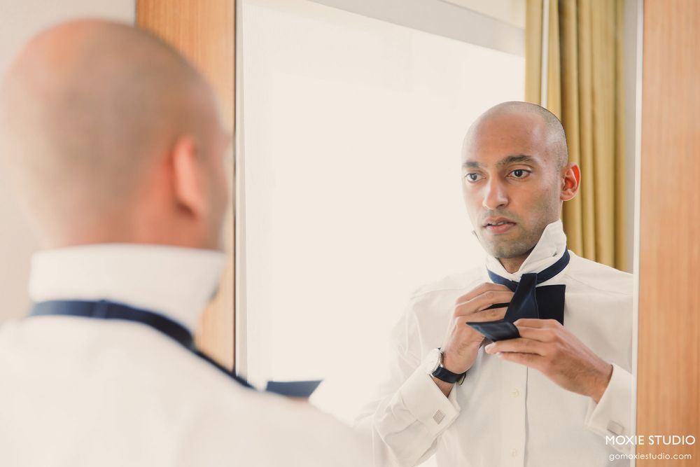 A person adjusts a bowtie while looking in a mirror during formal preparations.