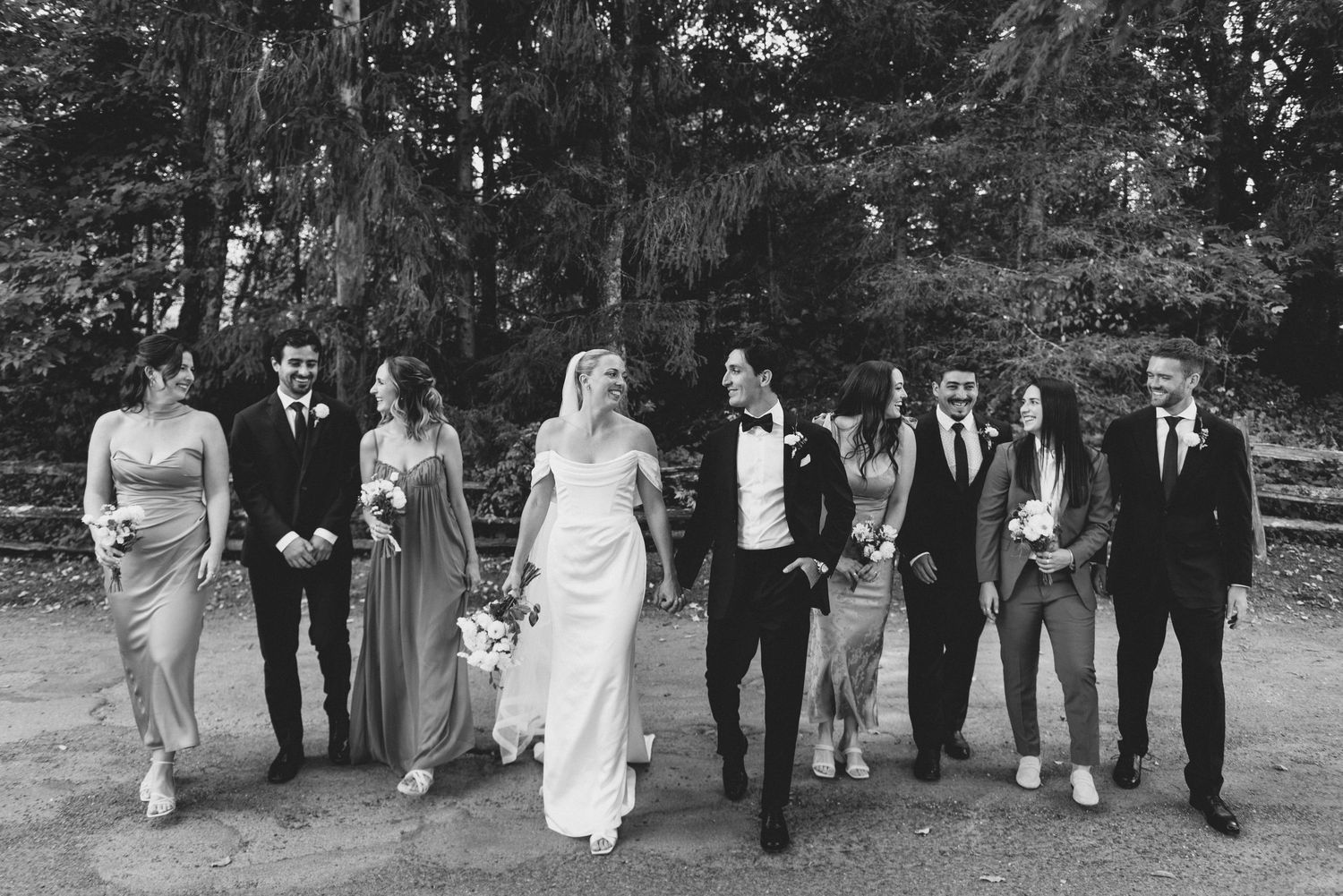 Wedding party walks together outdoors in a candid black and white photo series showing natural movement and joy.