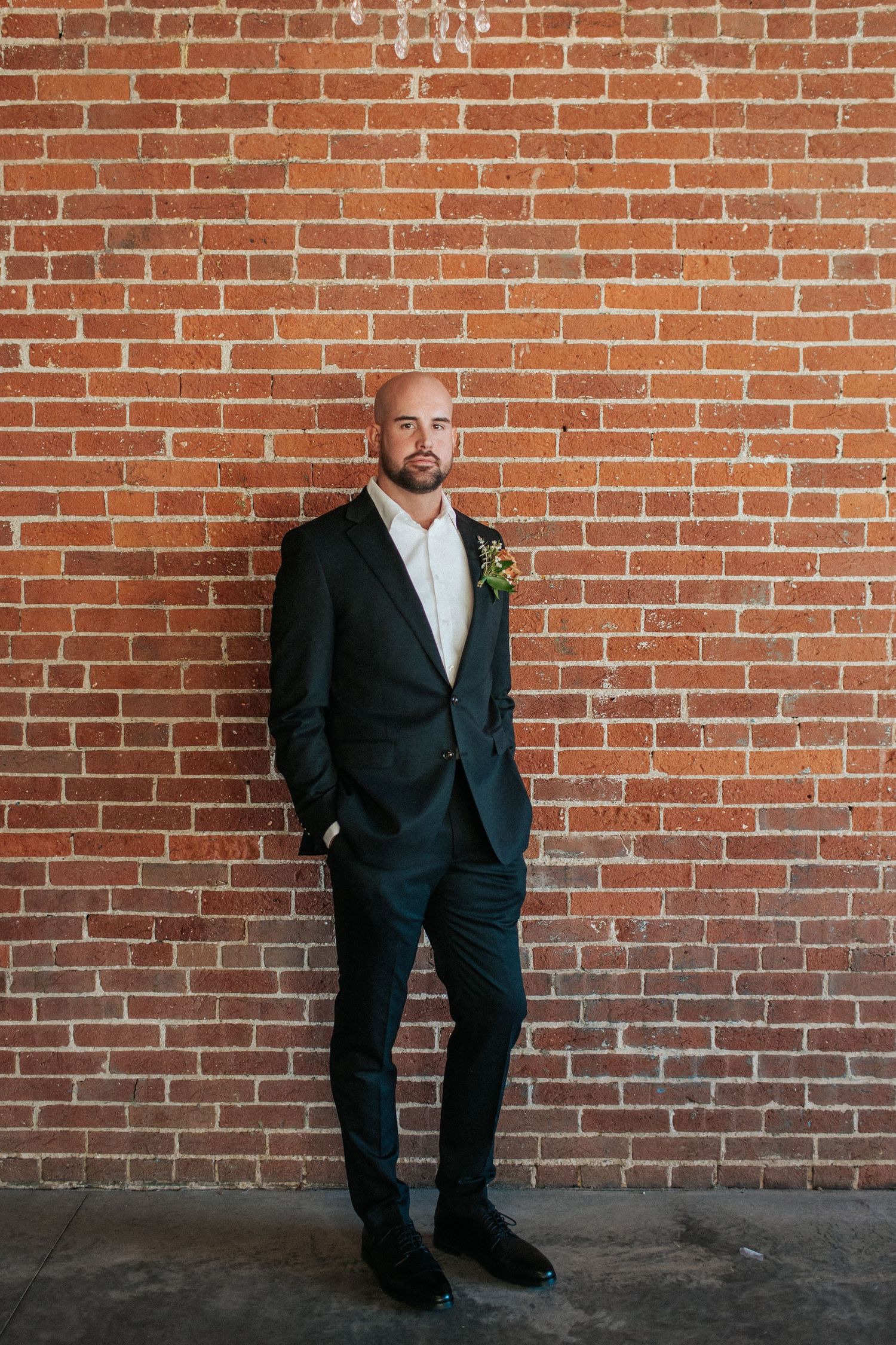 A formal black suit photographed against an exposed brick wall in an industrial setting.