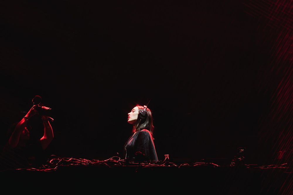 DJ performing at a dark concert venue with dramatic red lighting effects.