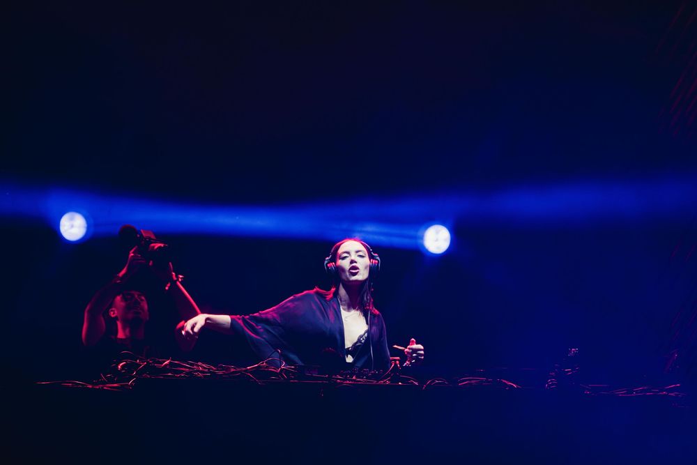 Stage lights illuminate a dark performance space with blue beams creating a dramatic atmosphere during a live show.