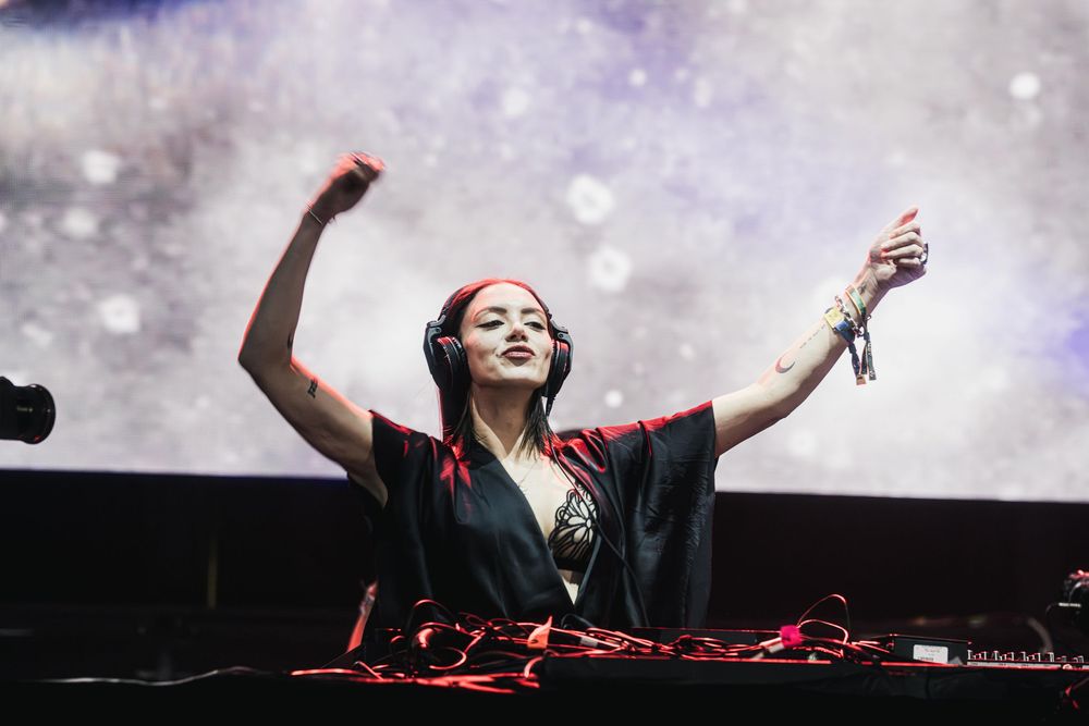 DJ performing on stage with dramatic lighting and snow effects at an electronic music concert.
