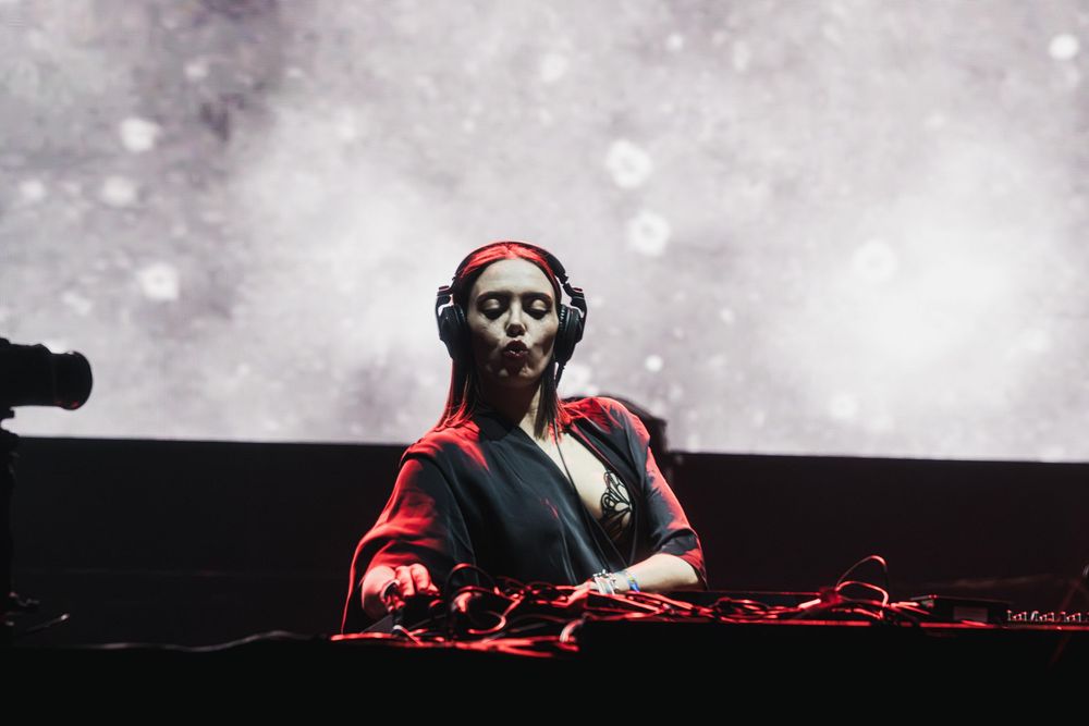 DJ behind turntables on stage with moody atmospheric lighting and fog effects.