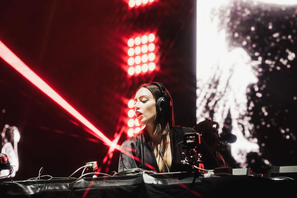 DJ performs at an electronic music concert with dramatic red lighting and stage effects.