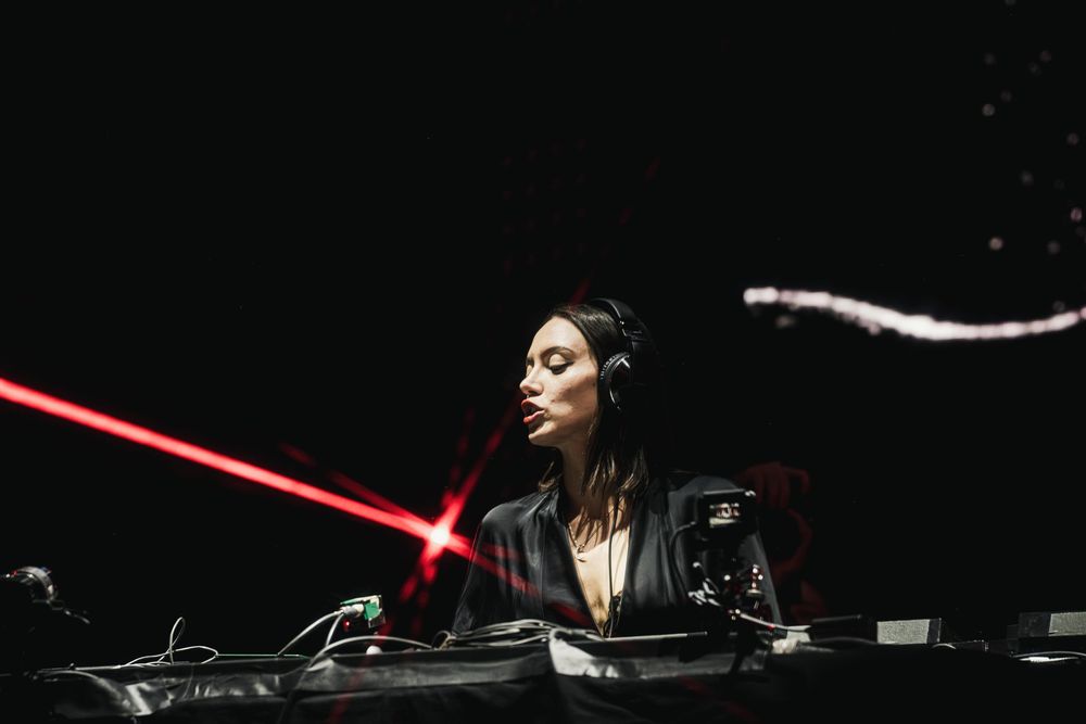 DJ performs at a turntable setup with red lighting effects in a dark nightclub atmosphere.