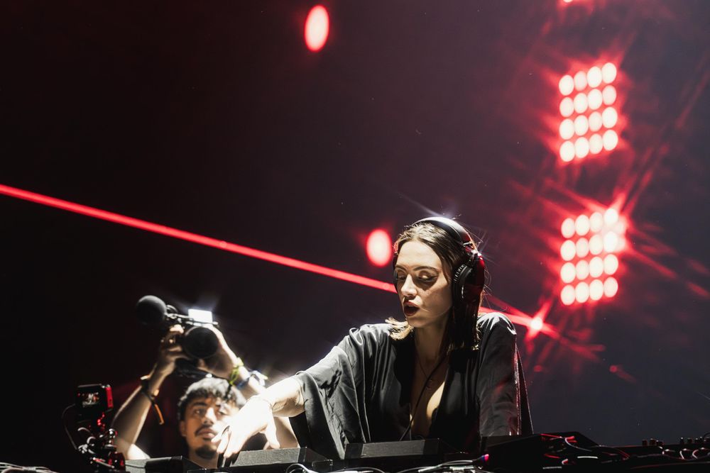 Concert performers on stage with dramatic red lighting and laser beams creating an atmospheric live music environment.