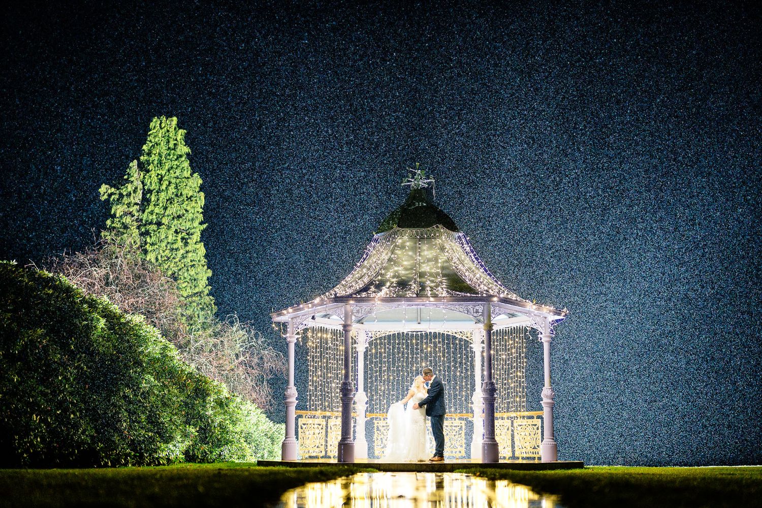 Nighttime wedding venue illuminated with string lights and gazebo against dark blue sky.