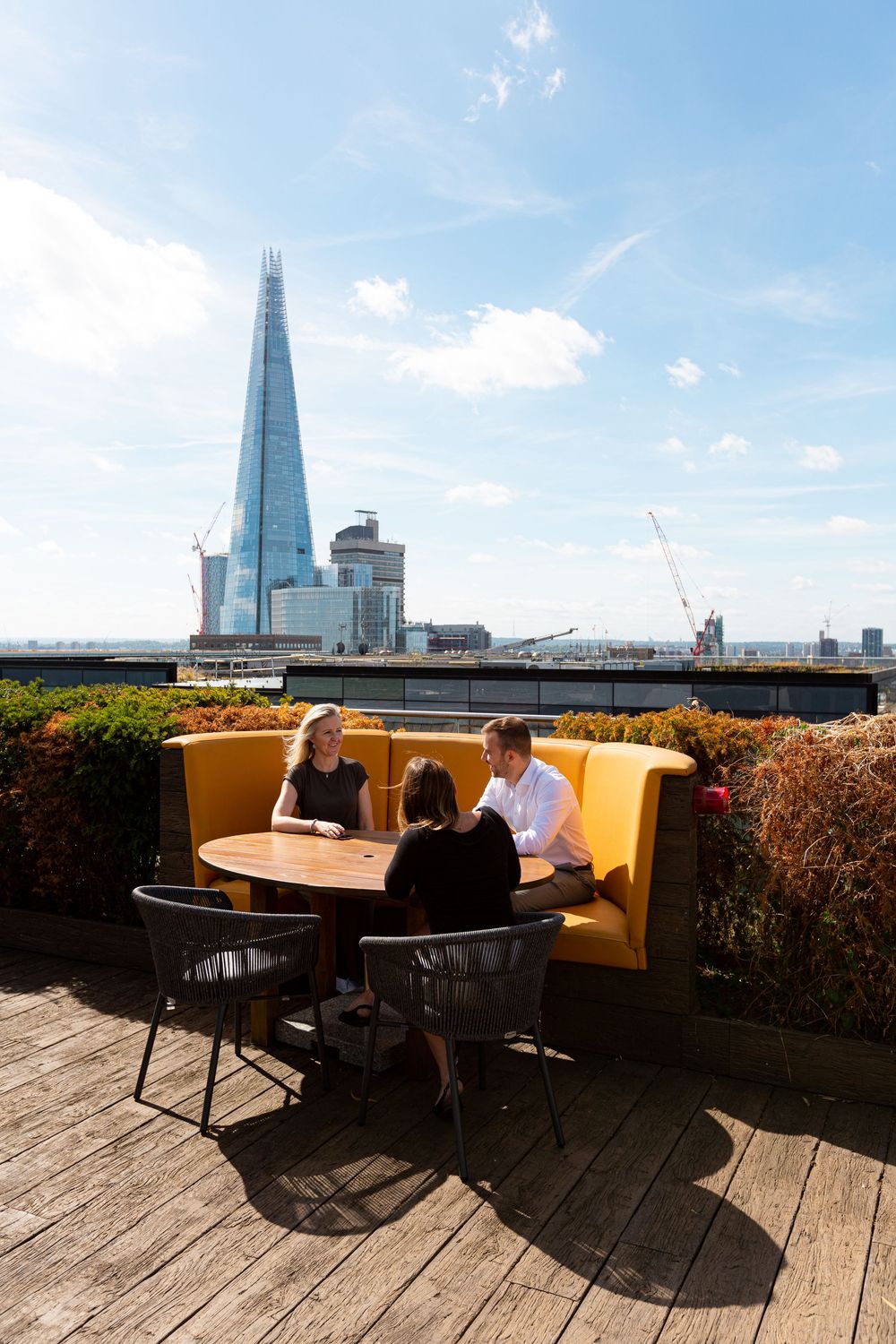 Outdoor rooftop terrace with wooden decking and seating areas overlooking The Shard building in London's skyline.