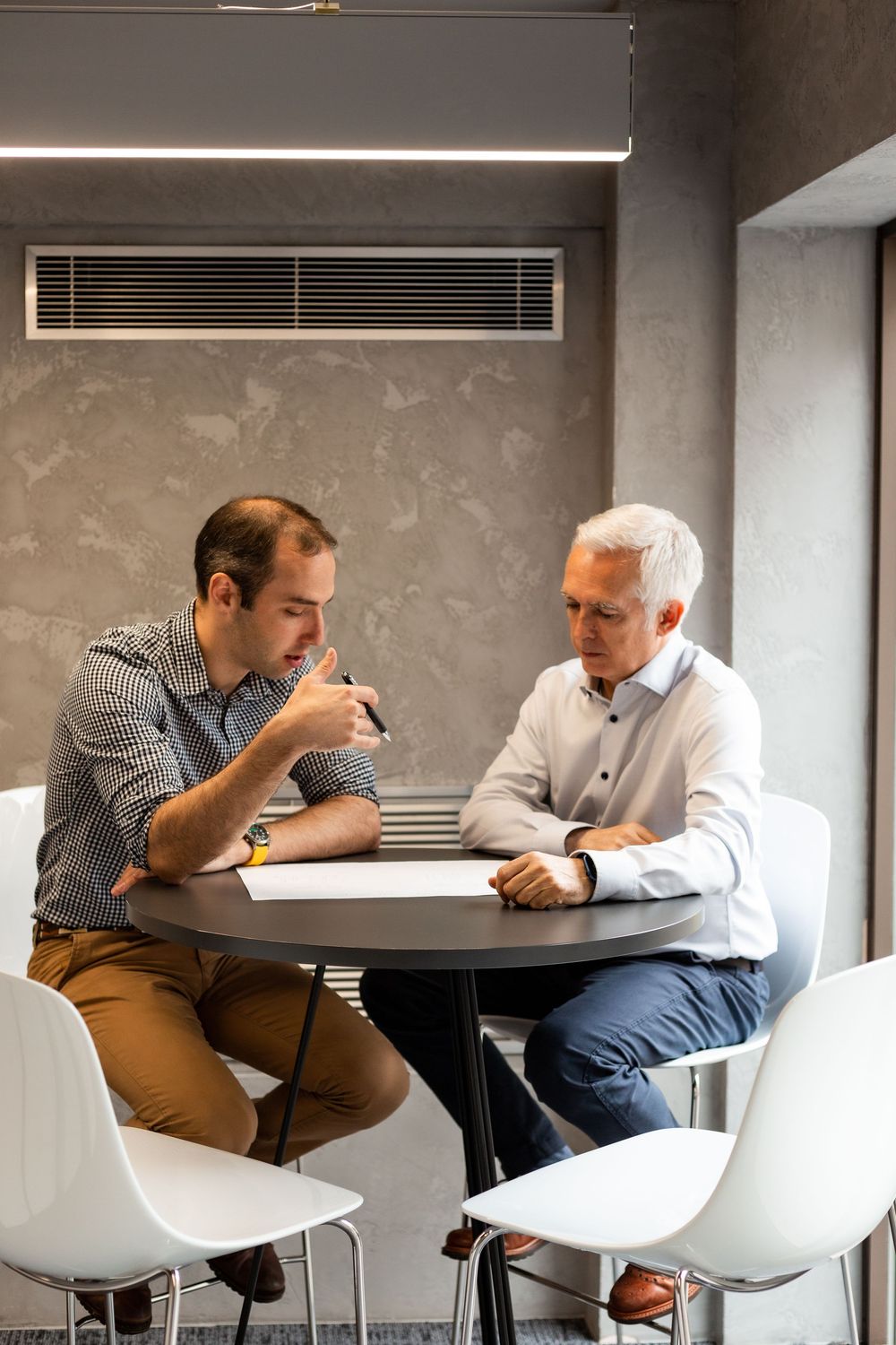 Business meeting at round table with white chairs in modern office setting.