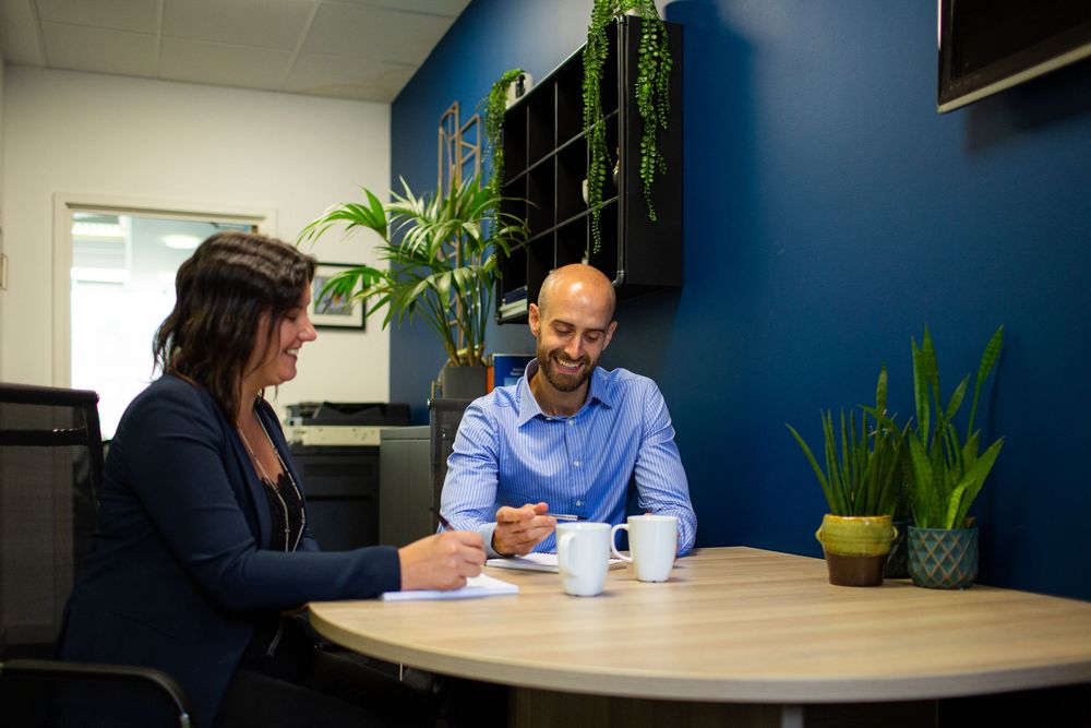 People collaborate at a modern office workspace with blue walls and white furniture during a business meeting.