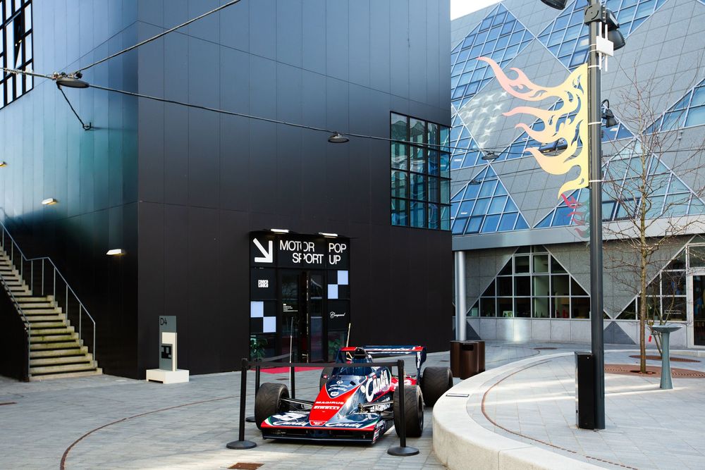 A Formula 1 race car displayed outside a modern motorsport museum with geometric architecture.