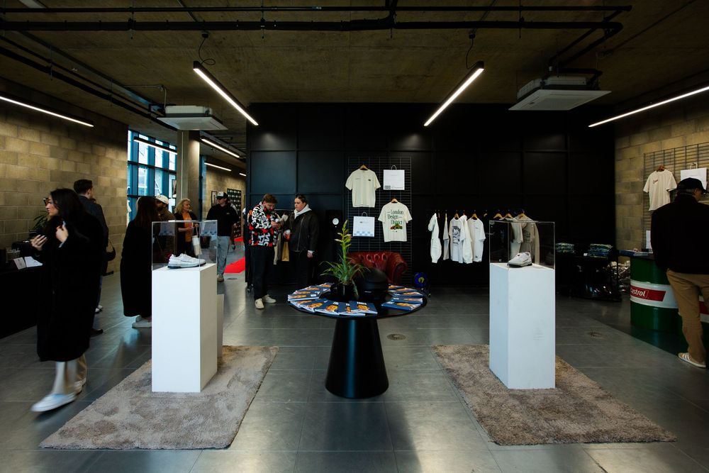 Modern retail pop-up showroom displaying white t-shirts and clothing on pedestals under neon lights with shoppers browsing.