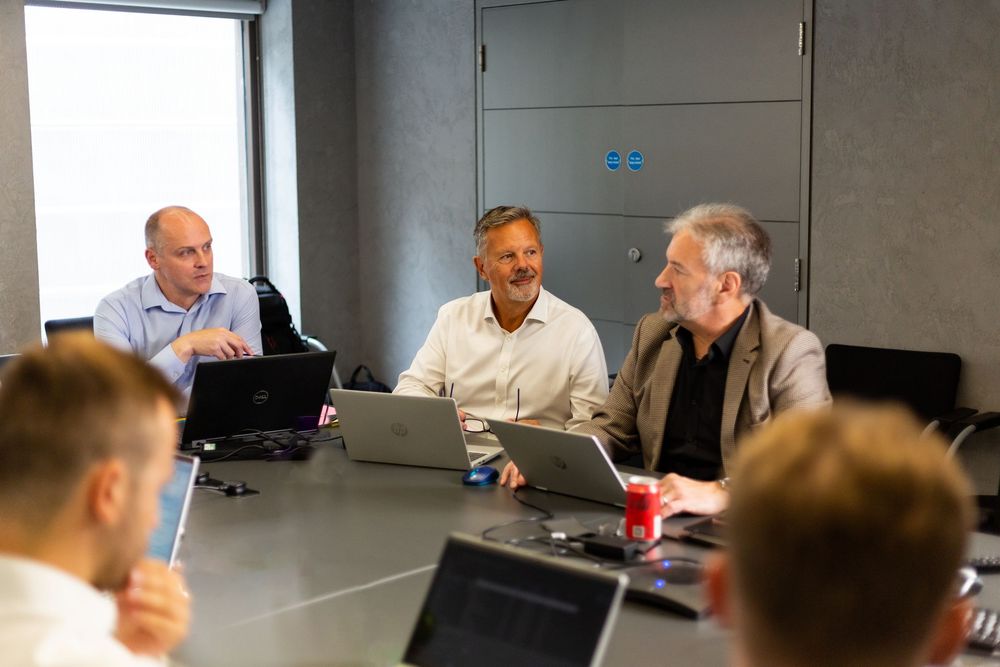 Business professionals gather around a conference table in a modern office meeting room for a discussion.