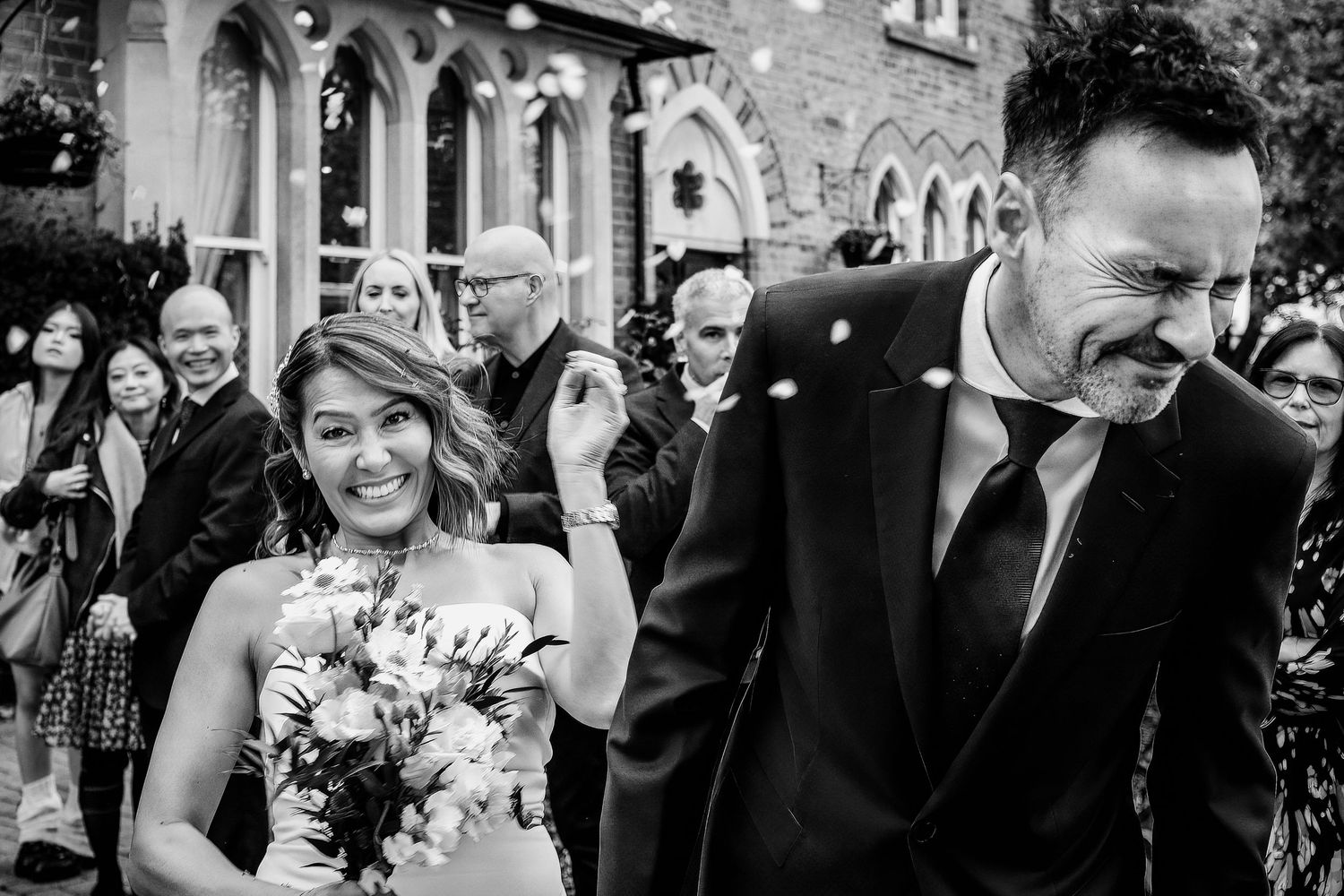 A black and white wedding photo showing a happy couple exiting a church building with guests in the background.