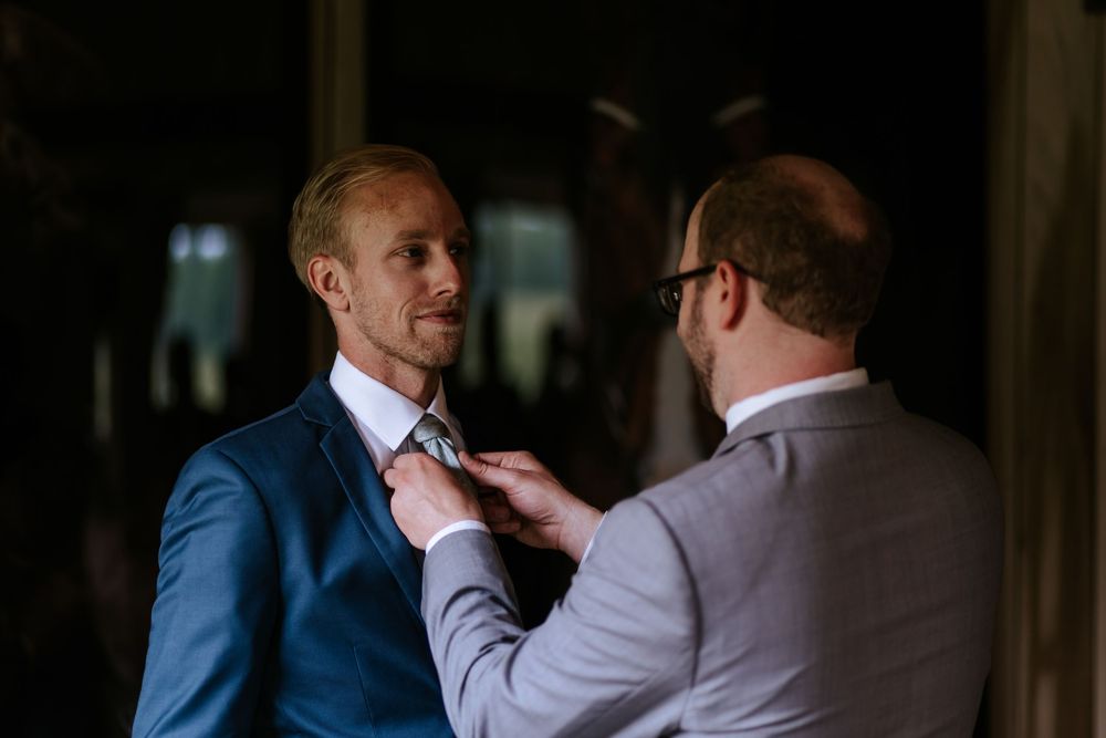 Men in formal attire adjusting clothing in a dimly lit room.