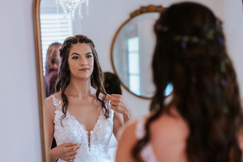 Bride getting ready in a white lace wedding dress with natural window lighting.