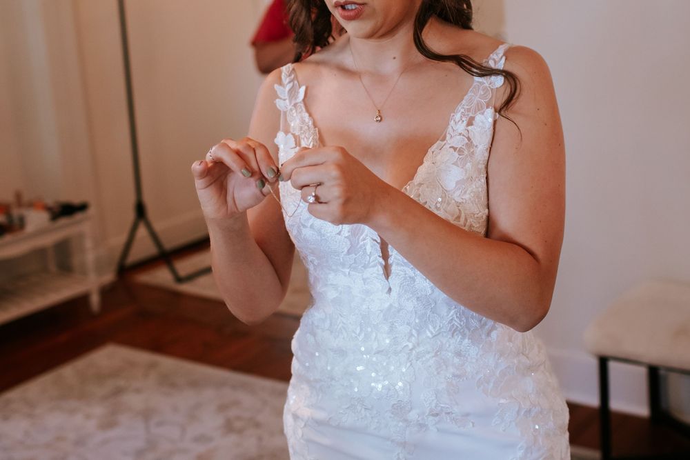 Bride adjusting wedding dress details in soft natural window light.