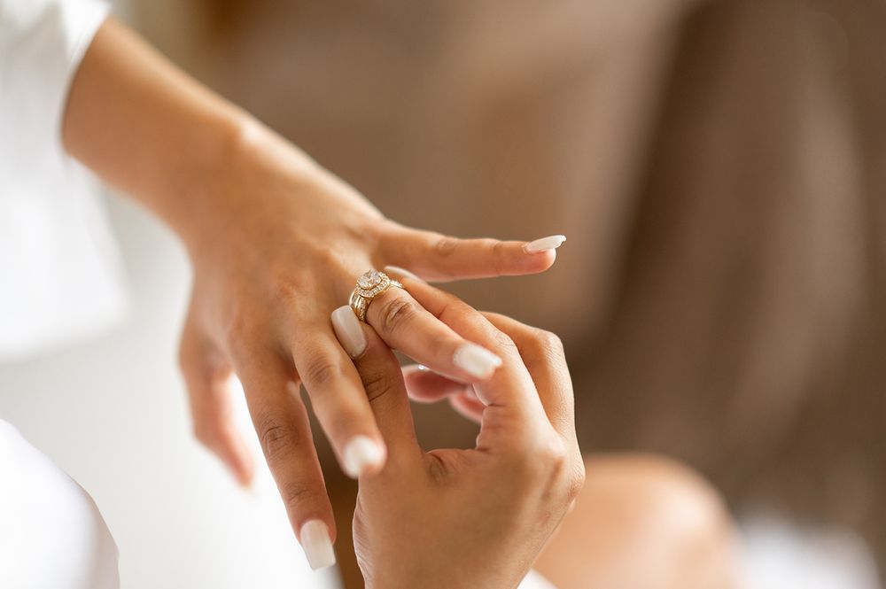 Close up of hands exchanging a diamond engagement ring in soft natural lighting.