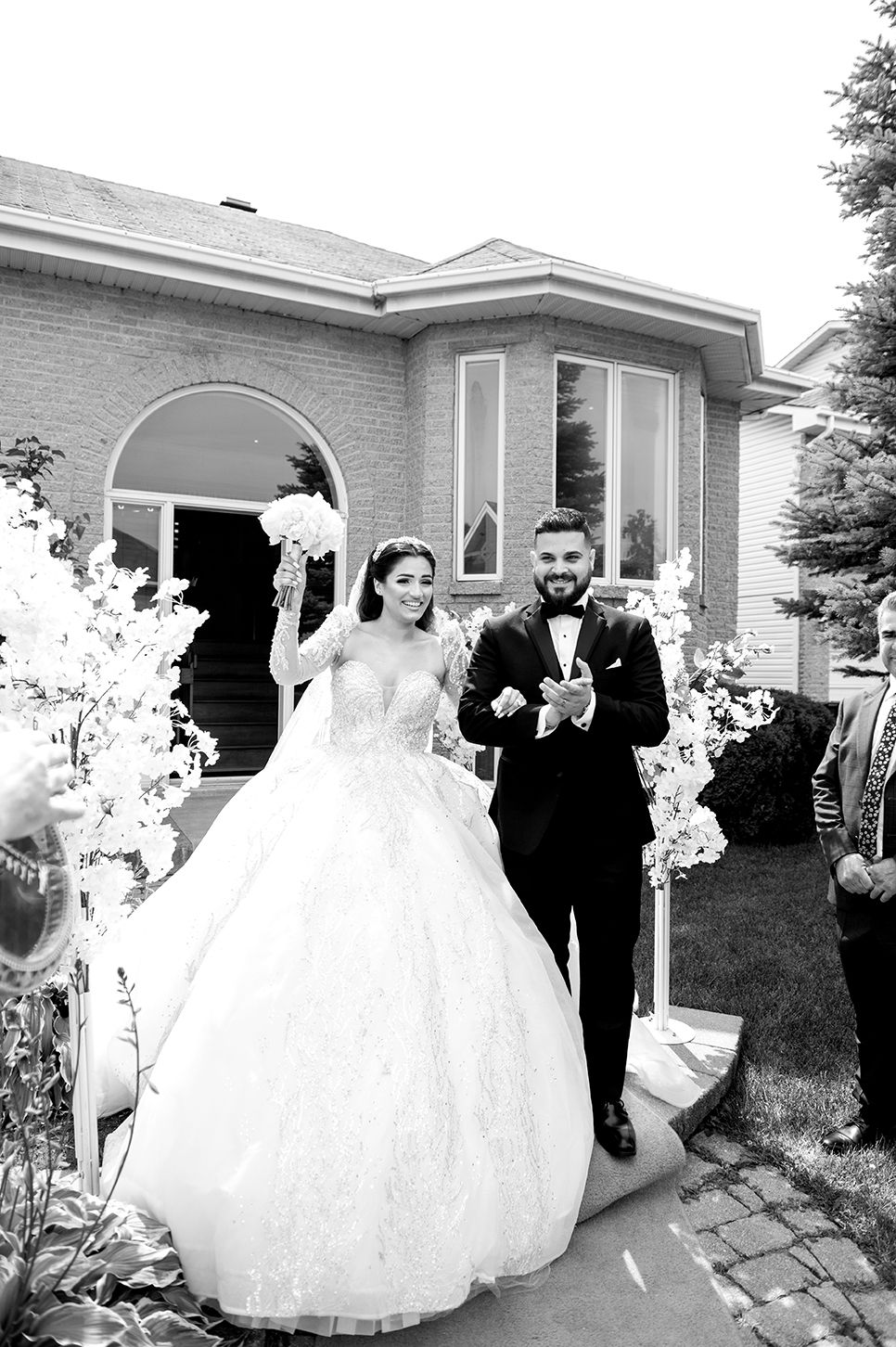 A wedding party walking outside a residential home with white decorative floral arrangements.
