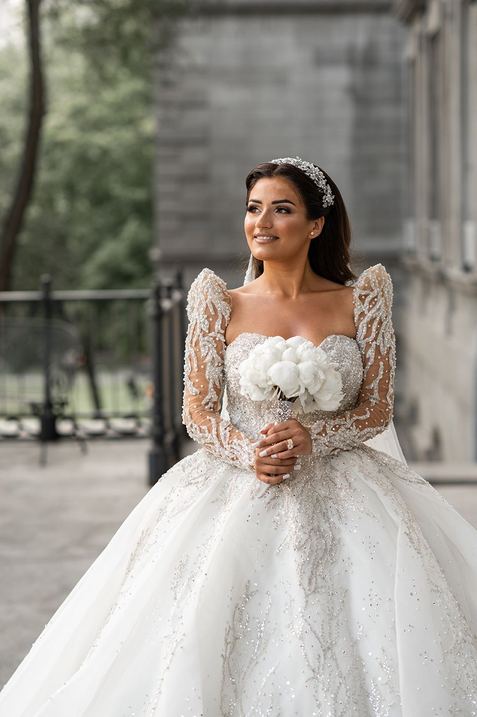 Stunning white ball gown wedding dress with intricate lace sleeves and sweetheart neckline shown in outdoor setting.