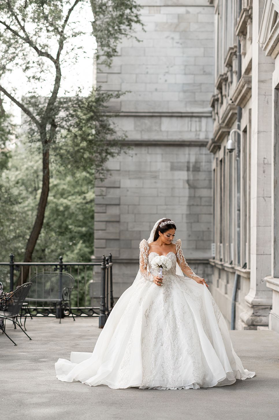 A bride in a stunning white lace ball gown poses in an elegant stone colonnade for wedding portraits.