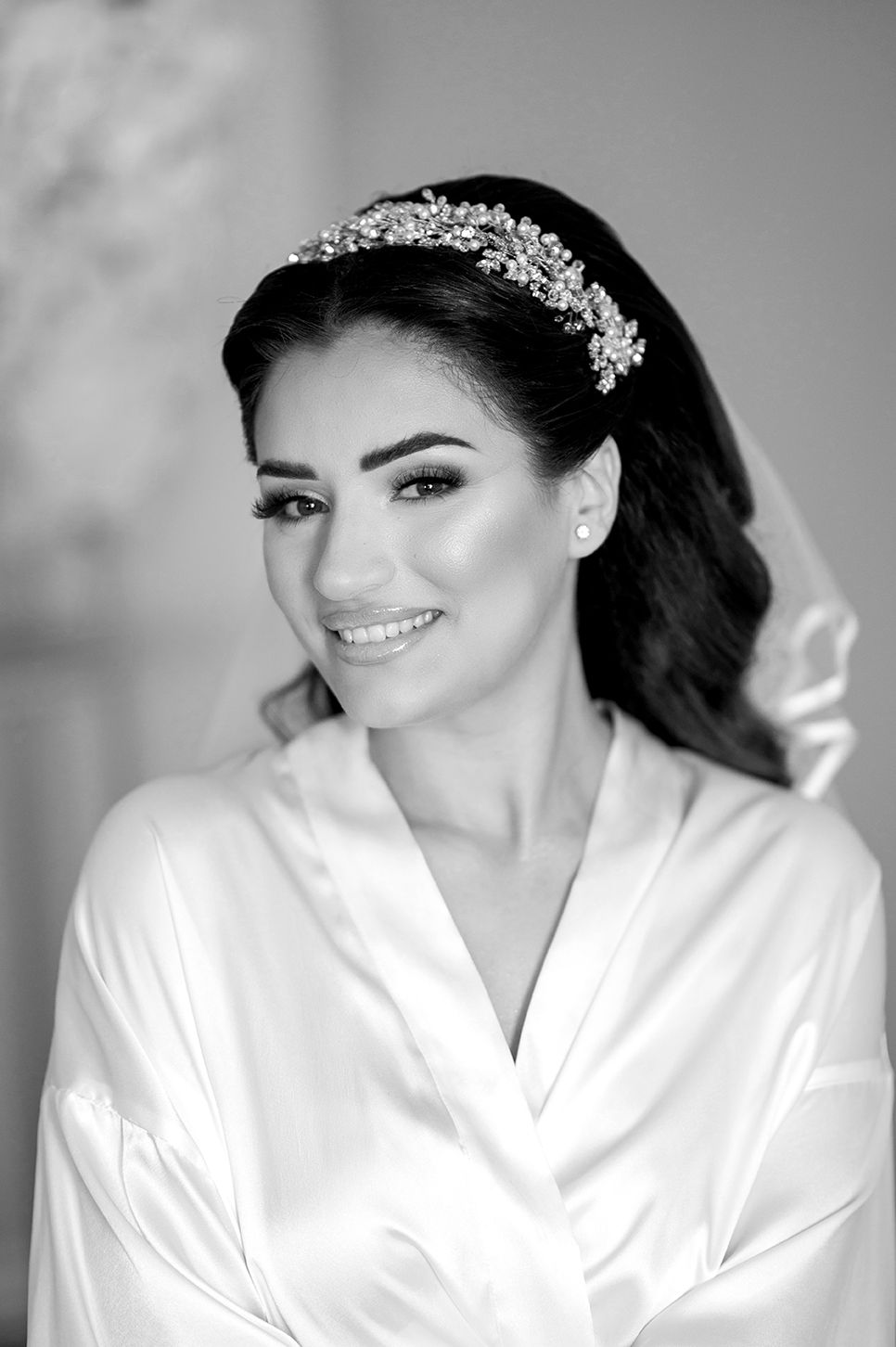 Black and white portrait of a bride wearing a silk robe and crystal tiara while smiling during wedding preparations.