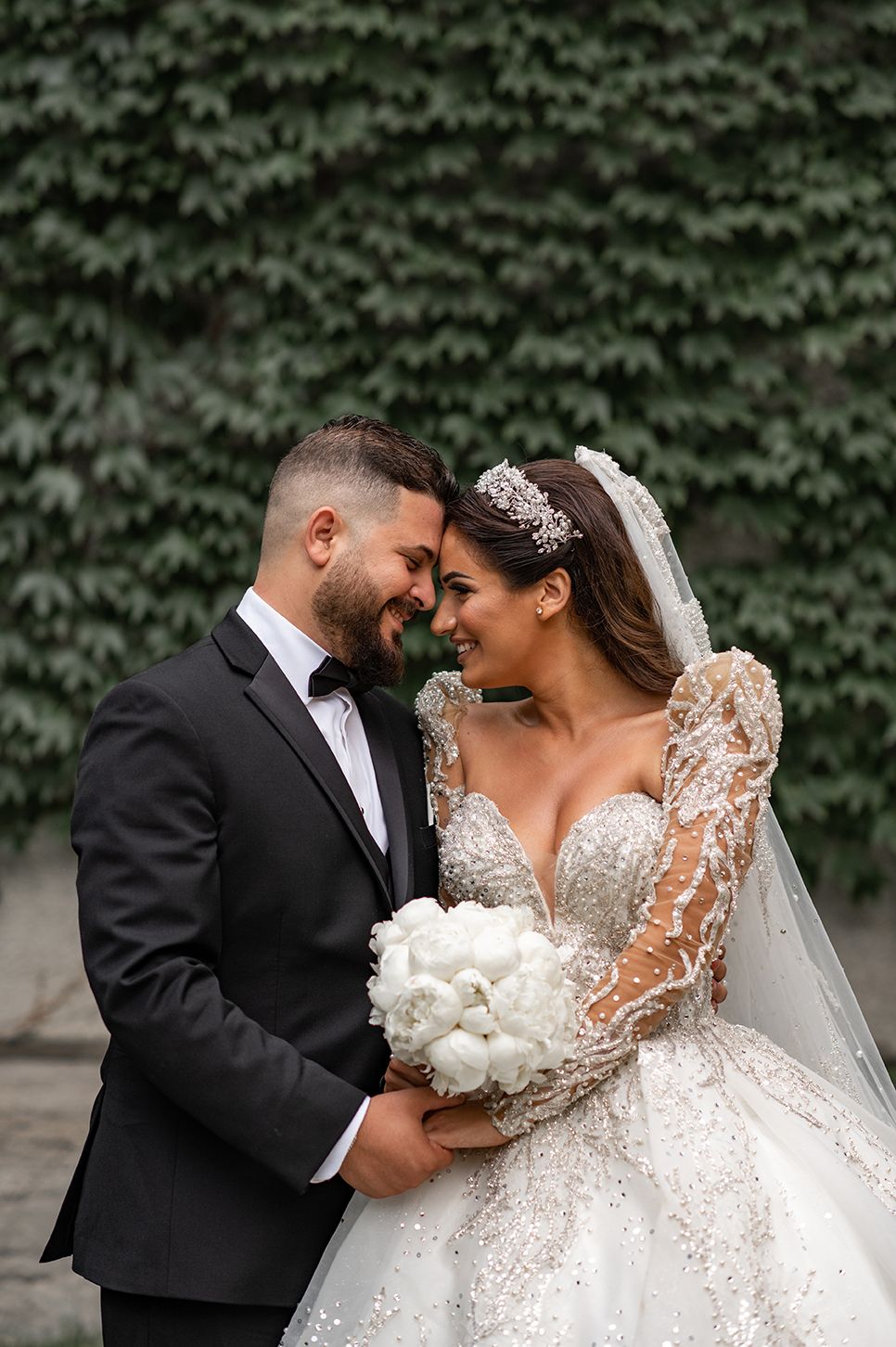 Romantic wedding couple sharing intimate moments in front of ivy-covered wall.