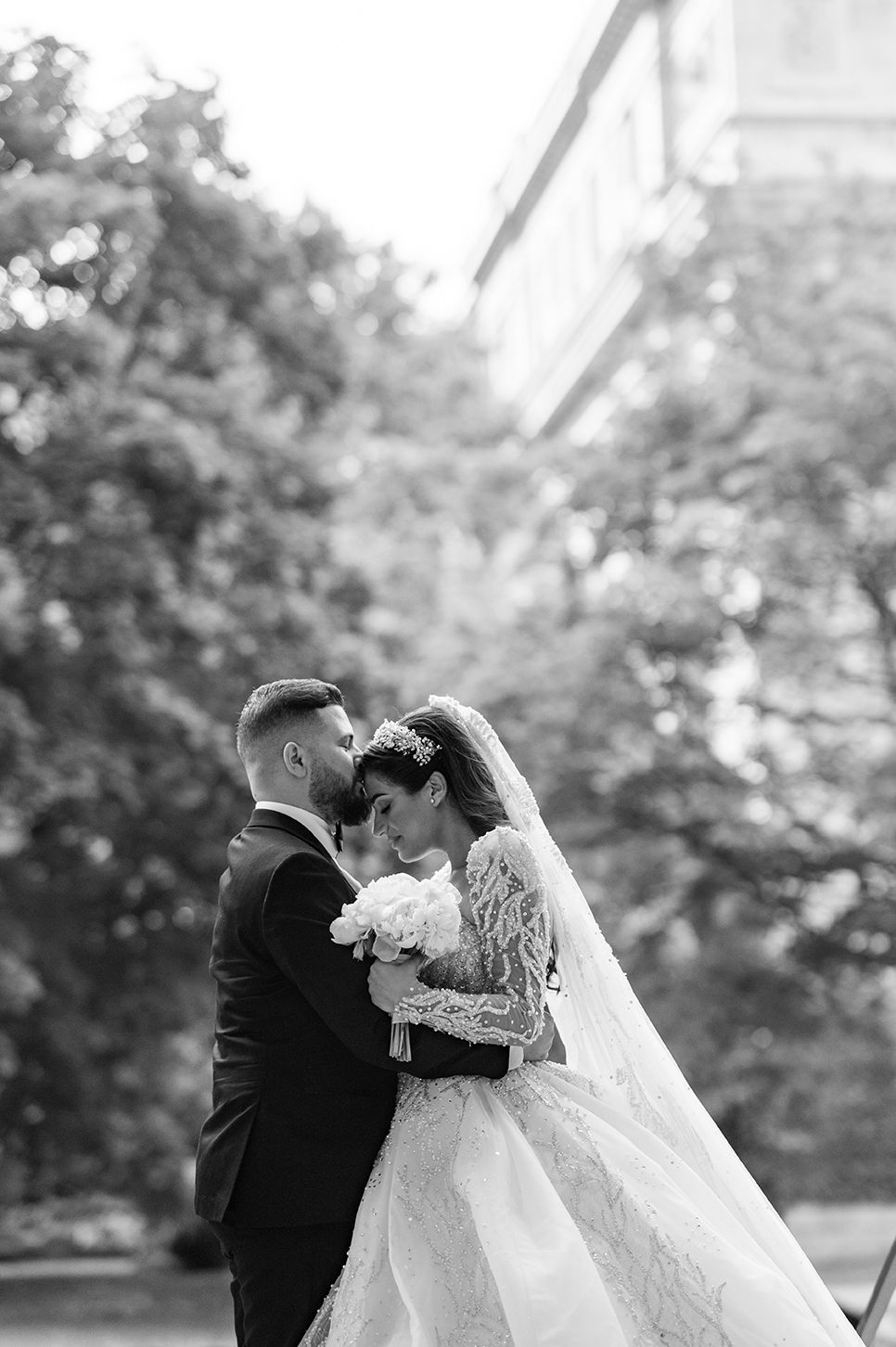 Black and white romantic wedding portrait captured outdoors with trees in the background.