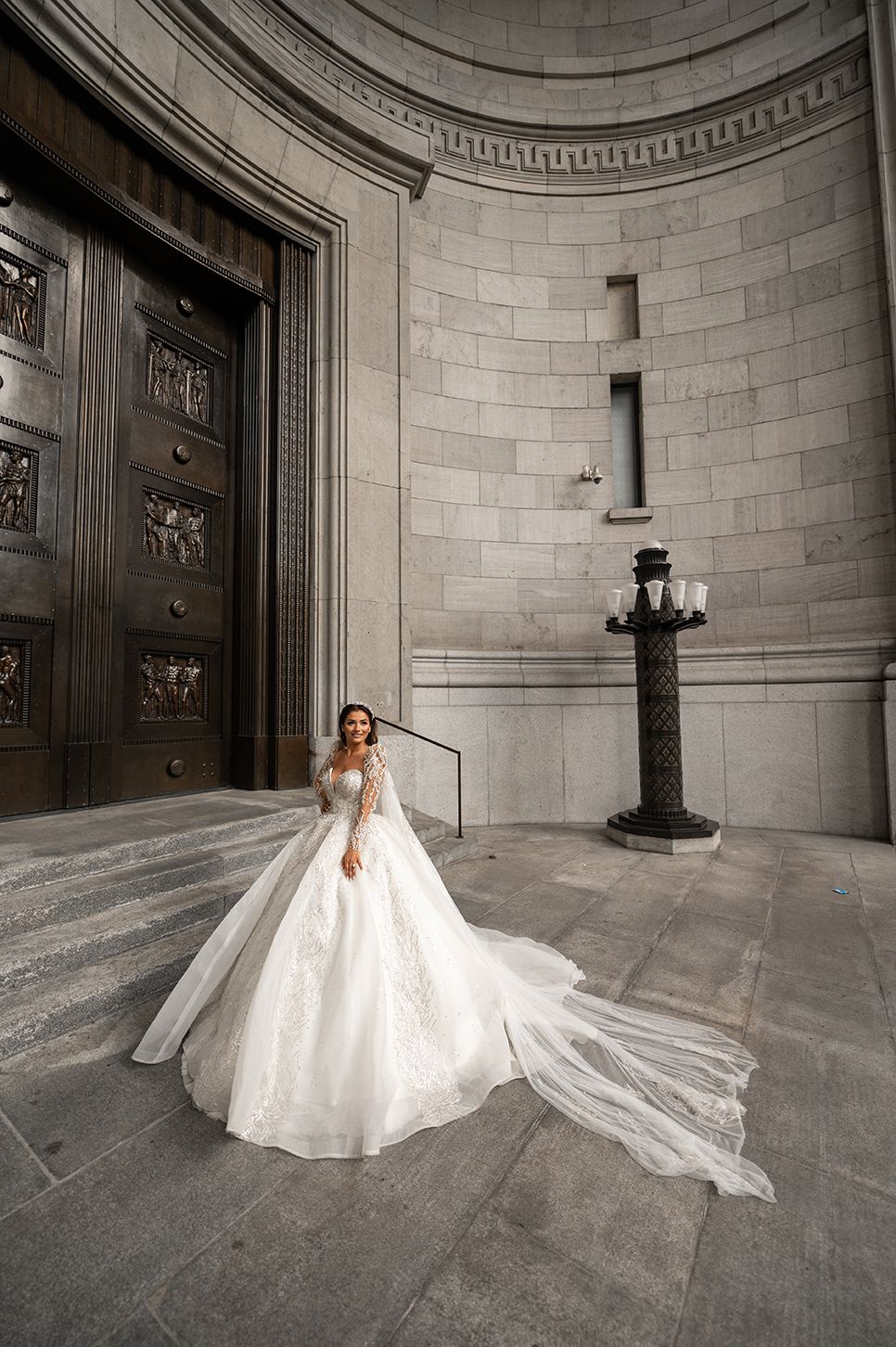 A bride in a flowing white ballgown with a dramatic cathedral veil poses in a grand marble rotunda.