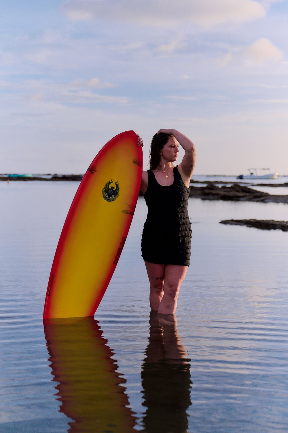 A surfboard and person stand in calm ocean waters at sunset creating a peaceful coastal scene.