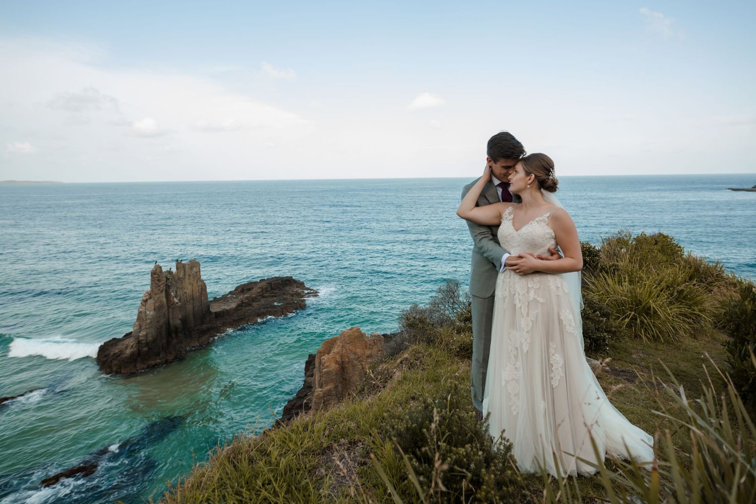 Bride and Groom on their wedding day Standing at a cliff's edge overlooking Cathedral Rocks in Kiama Downs, NSW