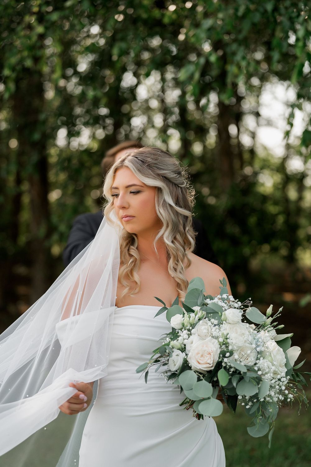 Bride holds elegant white and green bouquet while her veil flows in the breeze.