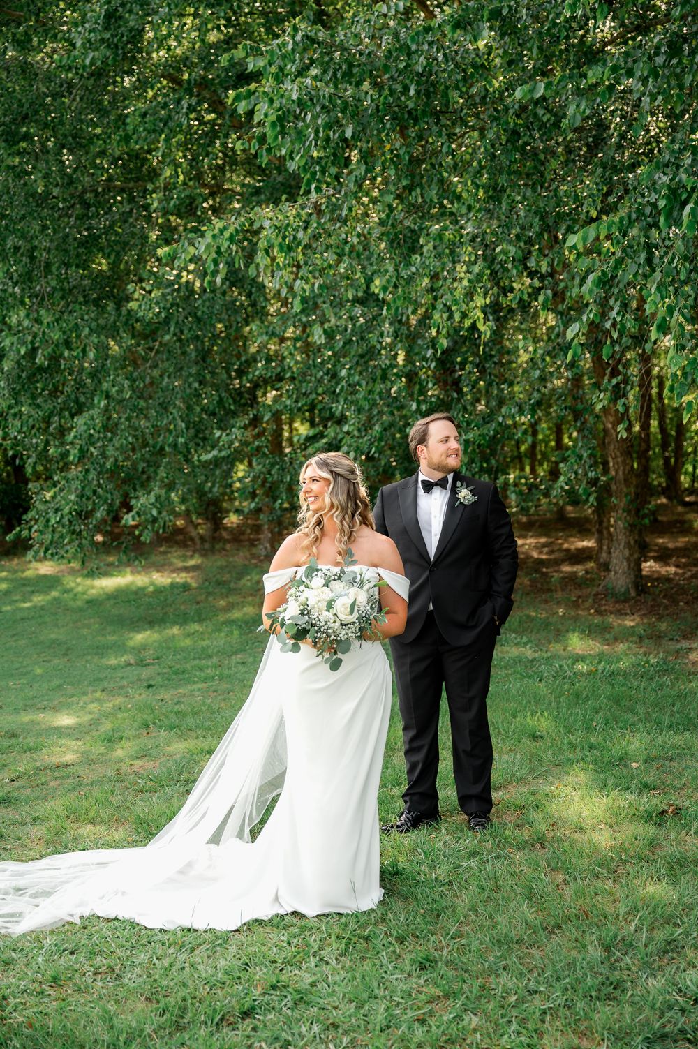Newlyweds pose together on grassy hill during outdoor wedding photoshoot.