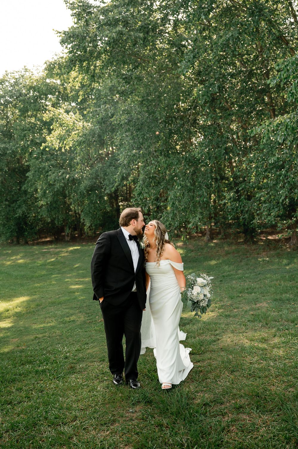 Newlyweds share an intimate moment on their wedding day surrounded by green trees.