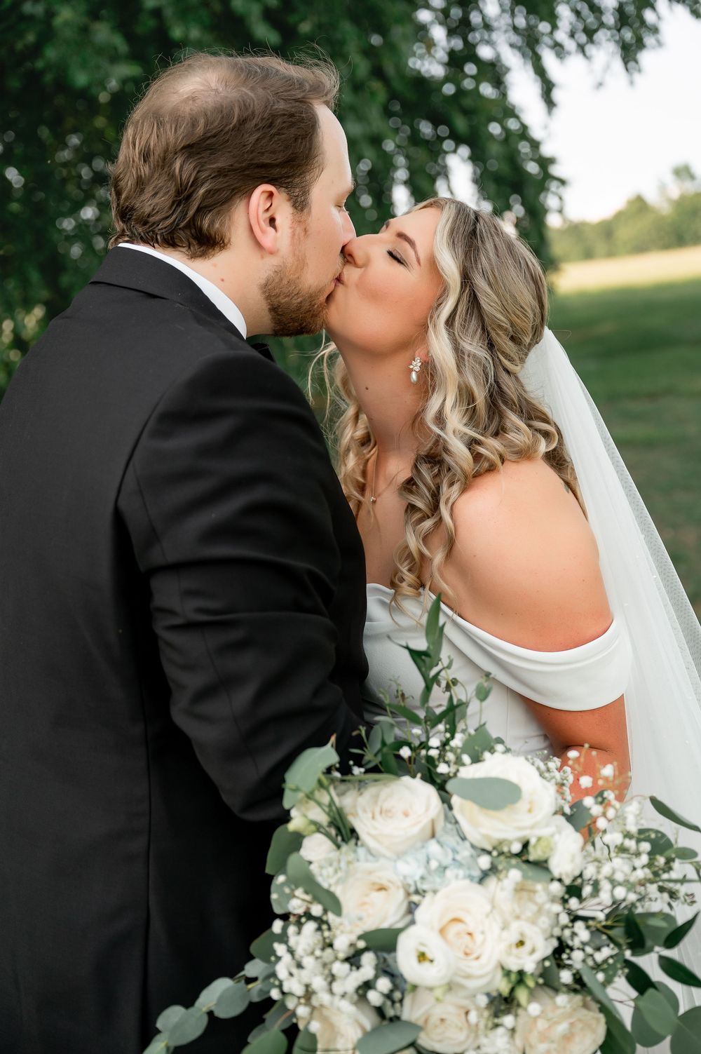 Intimate wedding photo of couple sharing a kiss while holding elegant white floral bouquet.