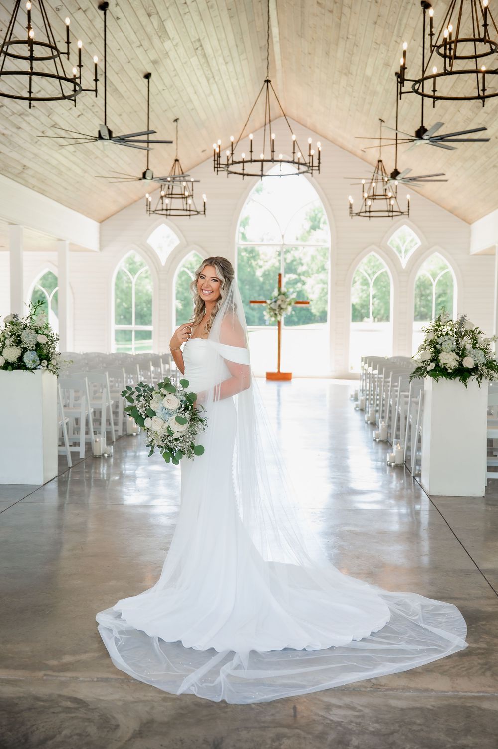 Stunning white wedding venue interior with vaulted ceiling, chandeliers and floral arrangements.