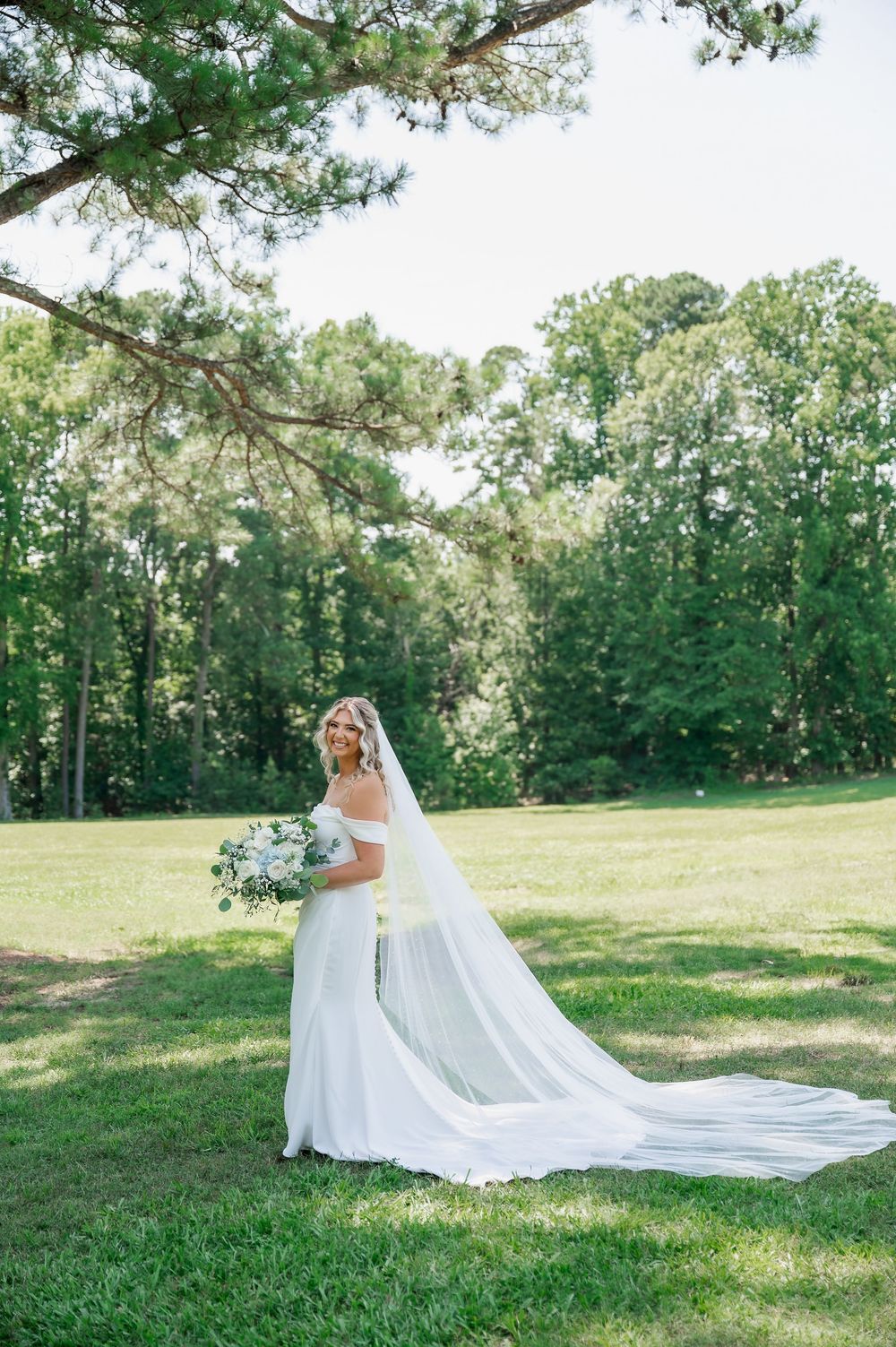 Beautiful wedding dress with flowing train photographed in a sunny outdoor field.