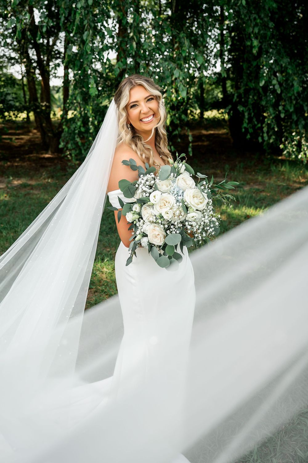 Bride in flowing white gown twirls her dress in an outdoor garden setting.