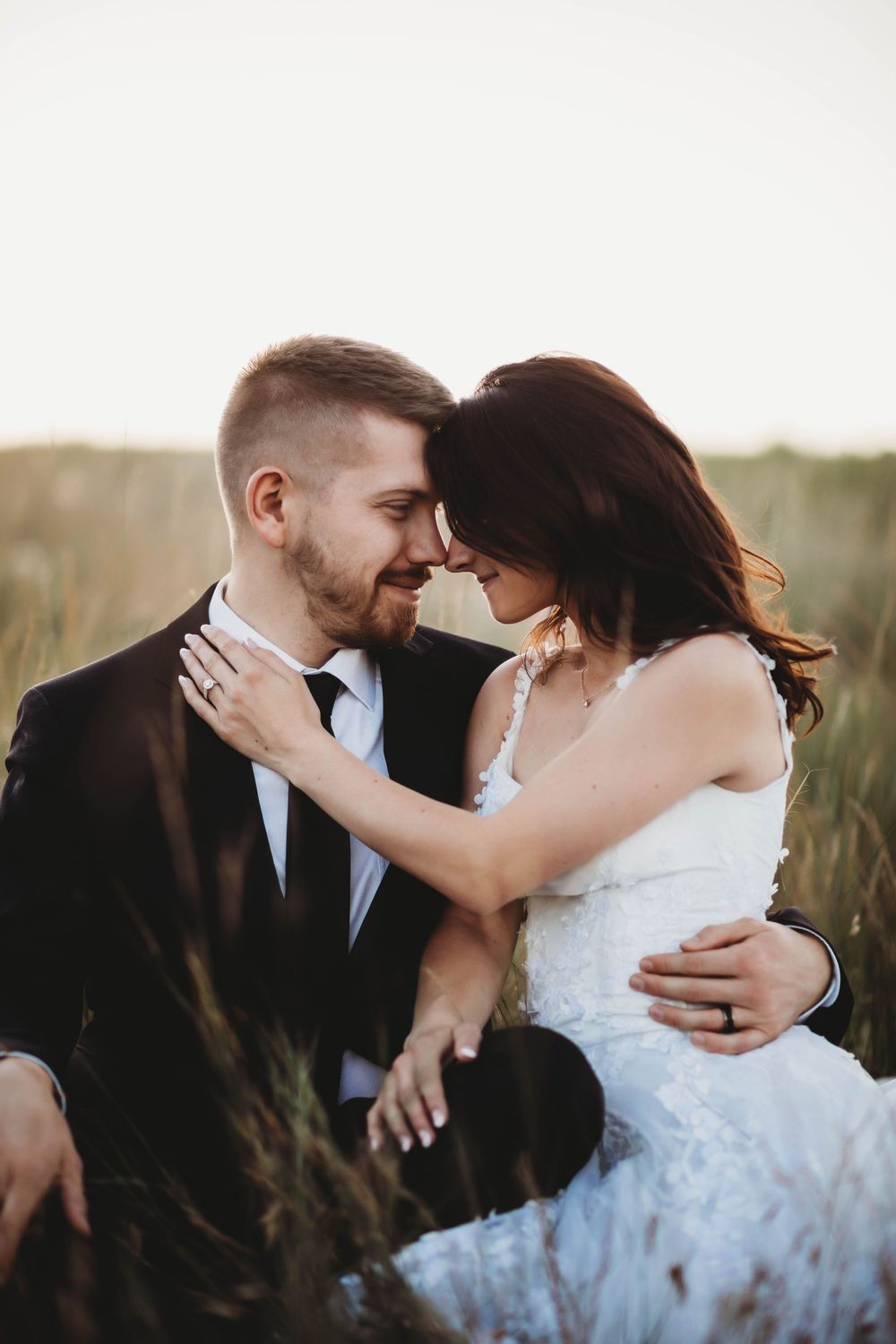 Intimate wedding couple moment captured in a field of tall grass during golden hour.