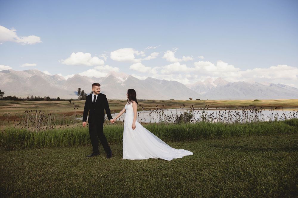 Wedding couple holding hands in front of snow-capped mountains and a serene lake.