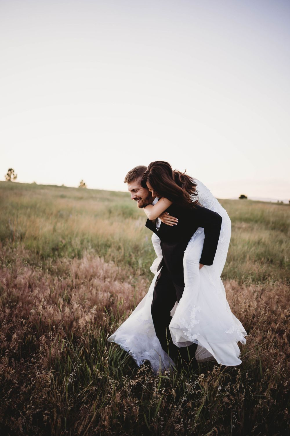 Wedding couple shares playful moments in a field during sunset.